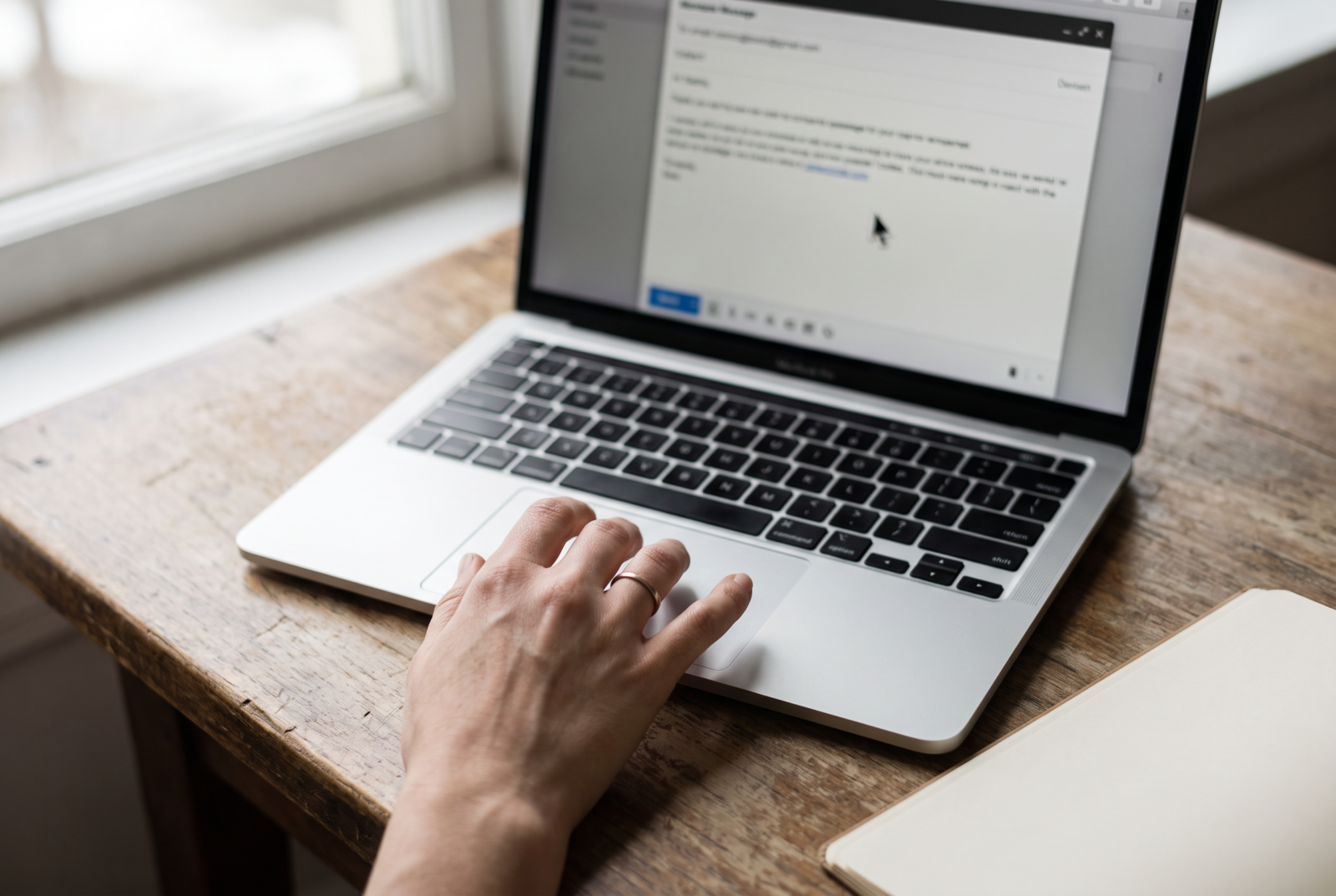 Close overhead shot of a hand hovering over a laptop trackpad, cursor paused on an unsent message, out of focus