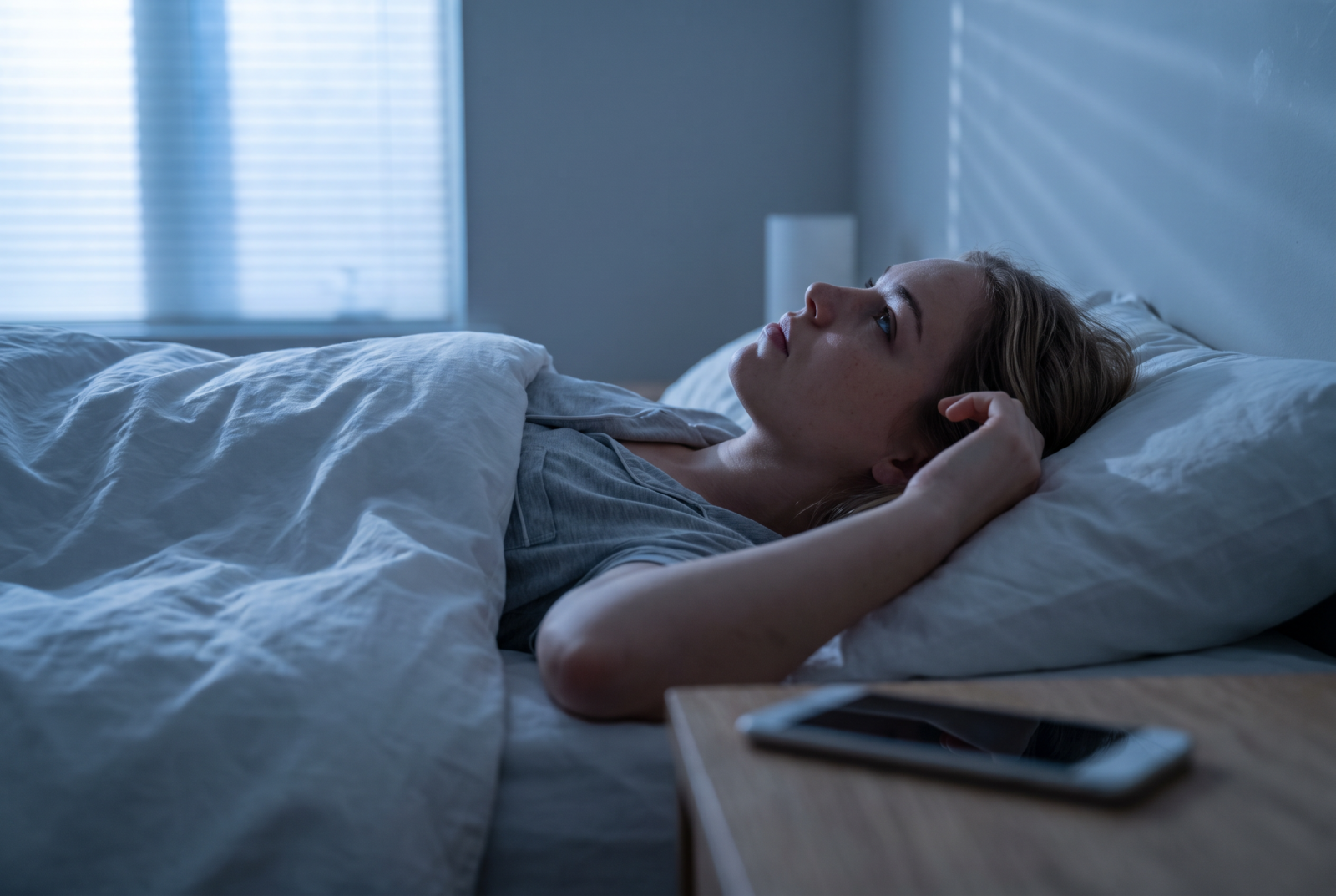 Vanesa lying awake in bed at blue hour, staring at the ceiling, phone face-down on the nightstand