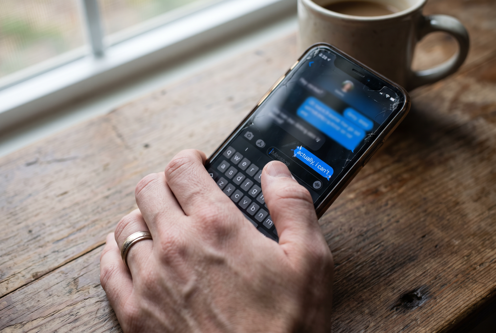 Close overhead shot of a hand holding a phone, thumb hovering over a text message, a partially typed and deleted message fading out mid-edit