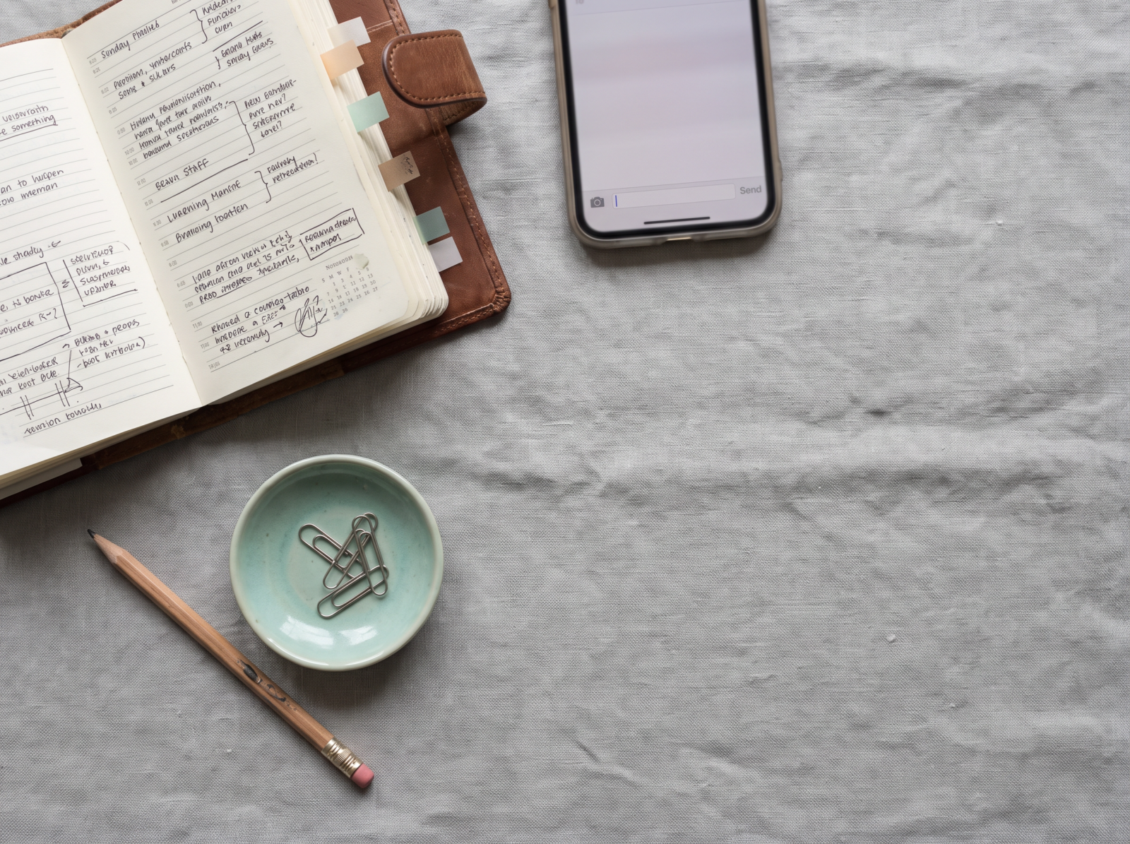 Flat lay of an over-scheduled planner, a worn-down pencil eraser, and a phone showing a blank unsent message draft