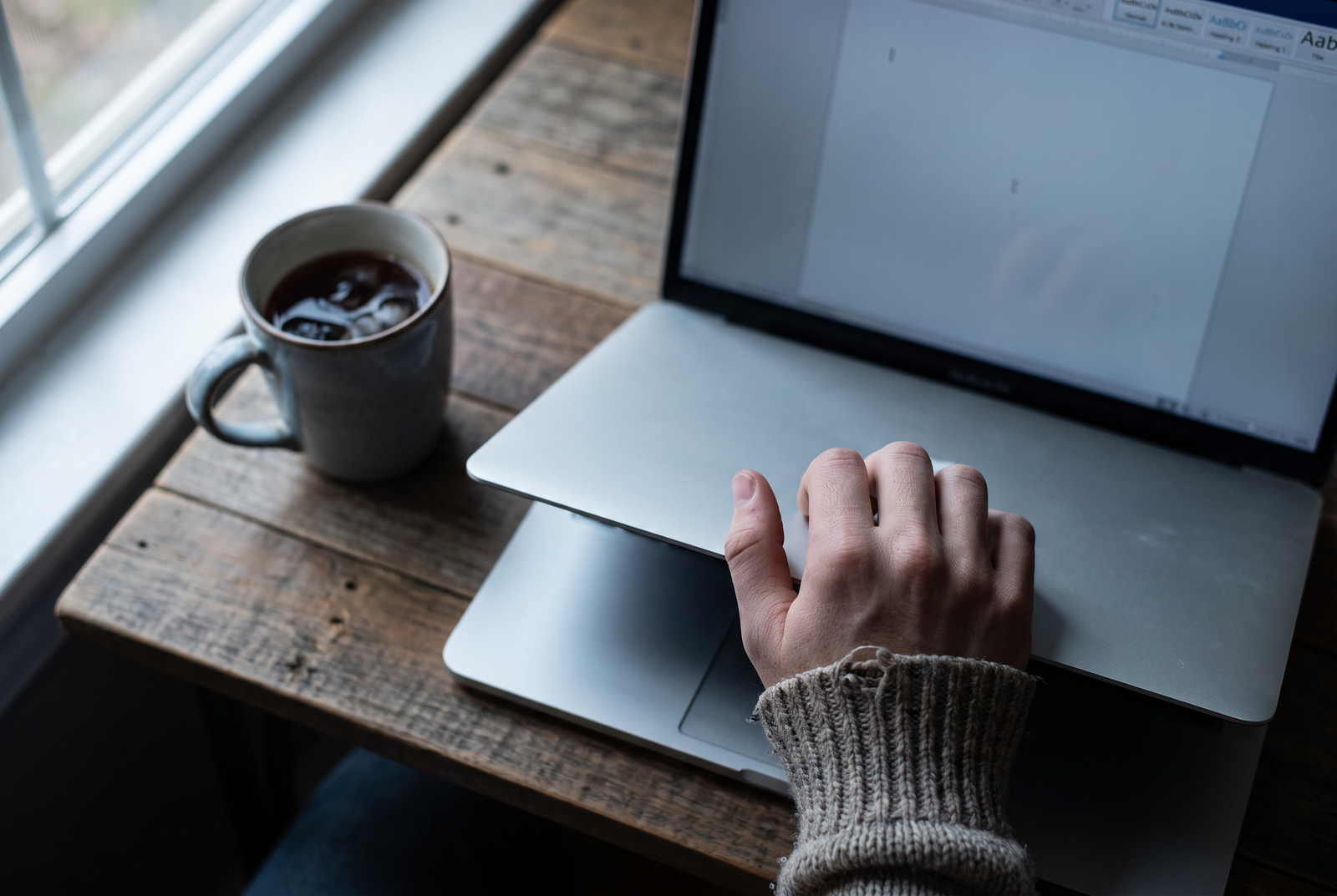 Close overhead shot of a hand hovering above a laptop about to close the lid mid-task, unfinished work visible but out of focus