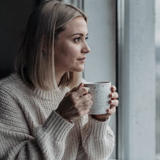 A woman holding a mug of coffee, looking out of a window